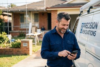 Artisan confirmant une prise de rendez-vous sur son smartphone devant un chantier de rénovation résidentiel