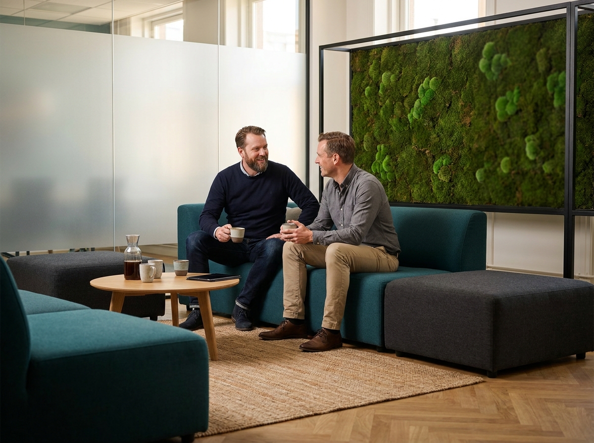 Deux collègues en conversation informelle dans un espace détente de bureau moderne avec mur végétal et mobilier modulable